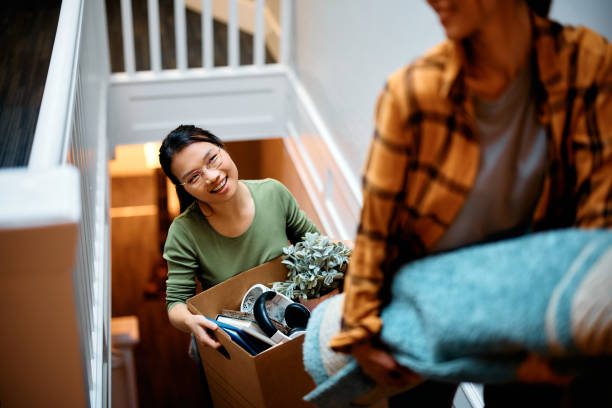 Young female friends walking up the stairs while carrying their belongings into a new home.